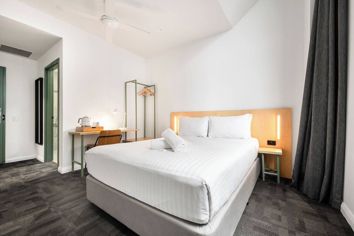 Una habitación de hotel con una cama grande, un escritorio con lámpara, una silla y una mesita de noche con lámpara.