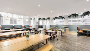 A spacious indoor dining area with wooden tables and benches, large windows, and potted plants. - YHA Sydney Central (Haymarket)