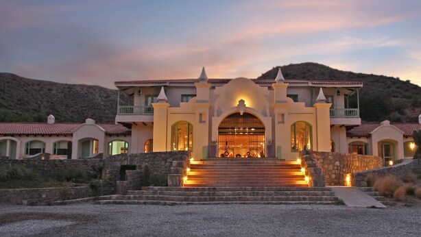 A large, multi-story building with a central entrance flanked by two wings, set against a hilly backdrop. - Hotel Huacalera (Huacalera)