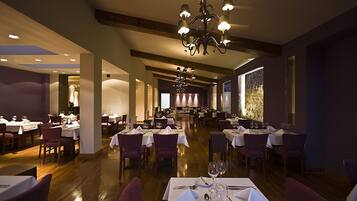 Een ruime restaurantruimte met meerdere tafels en stoelen, een kroonluchter en een houten plafond.