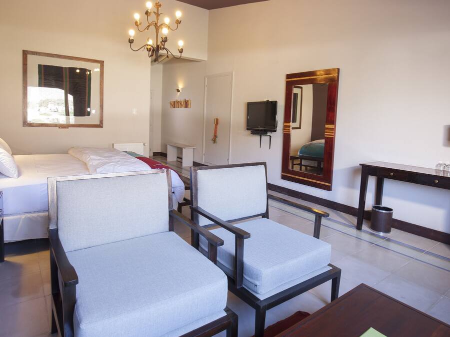 Habitación de hotel con cama, dos sillones, escritorio, televisor, espejo y candelabro.