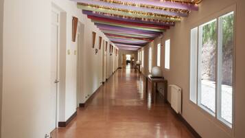 A long, narrow hallway with wooden floors and white walls, featuring a series of doors on one side and large windows on the other.