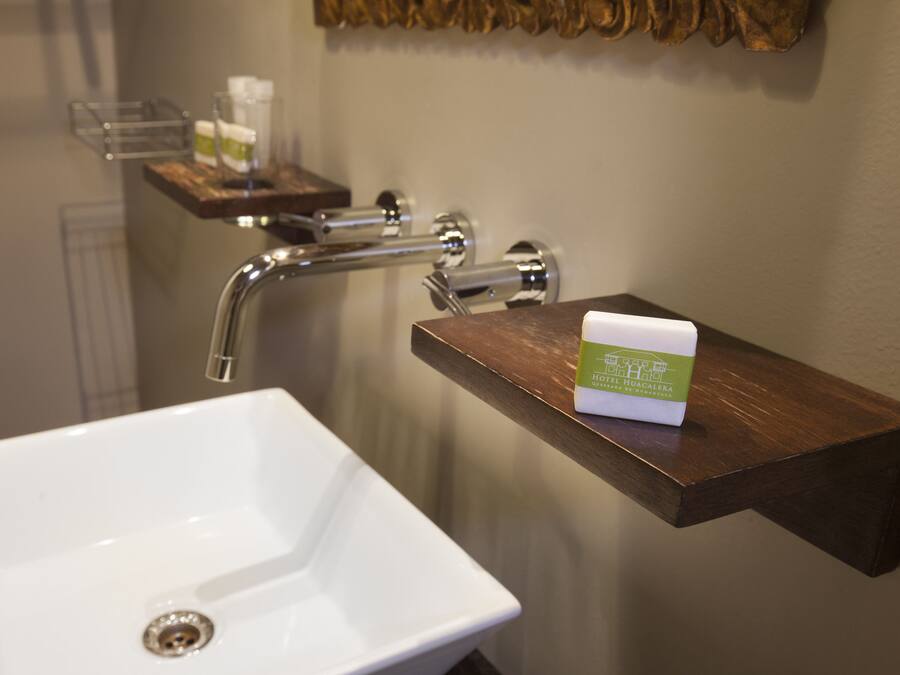 Un baño con un lavabo blanco, un tocador de madera y un dispensador de jabón sobre el tocador.