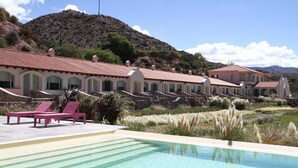 A pool area with lounge chairs and a building with a red-tiled roof. - Hotel Huacalera (Huacalera)