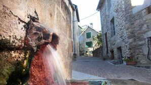 Une rue étroite, avec un bâtiment en pierre sur la gauche et un élément décoratif aquatique au premier plan.