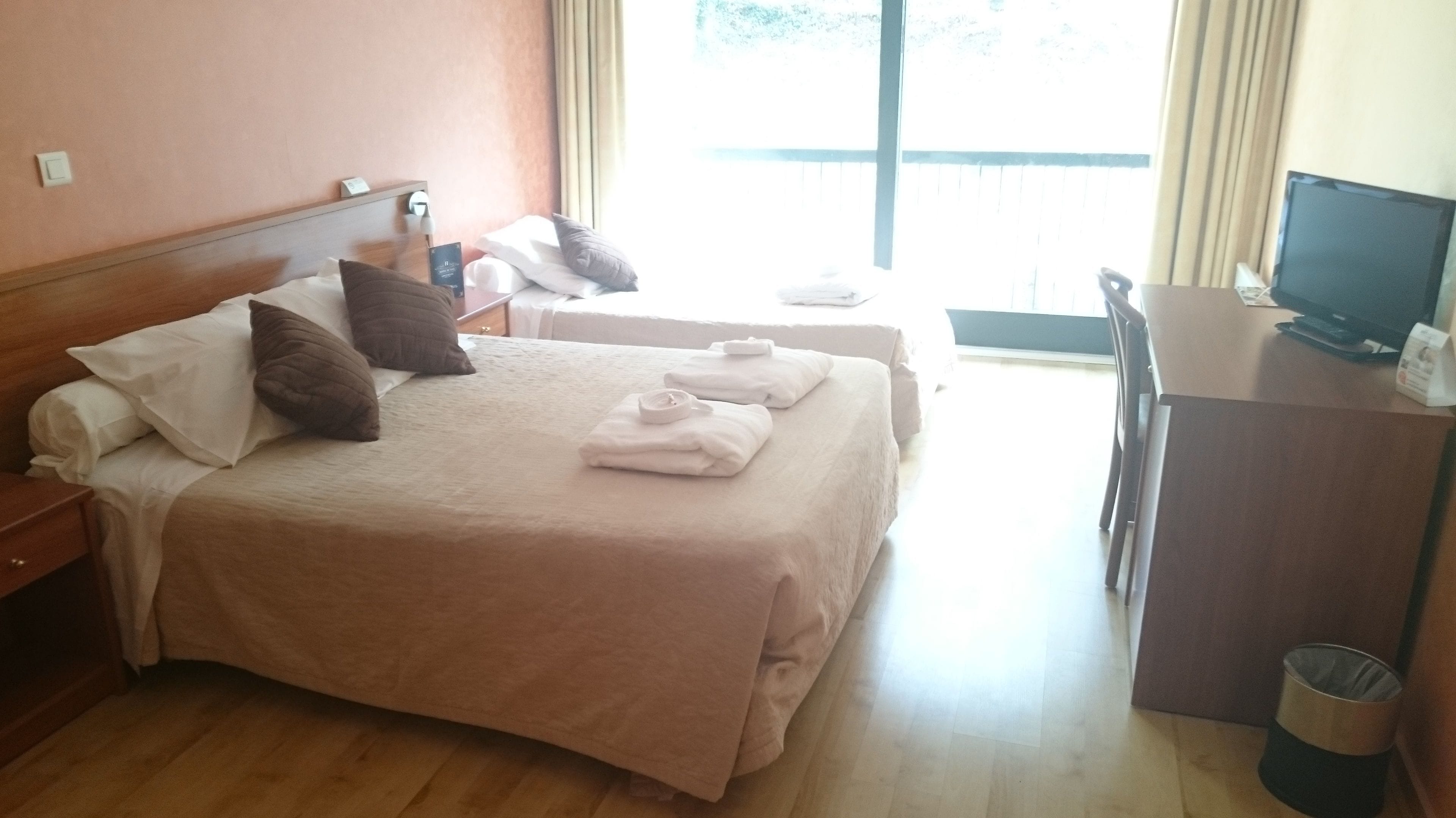 A hotel room with two beds, a desk, a television, and a window with curtains.