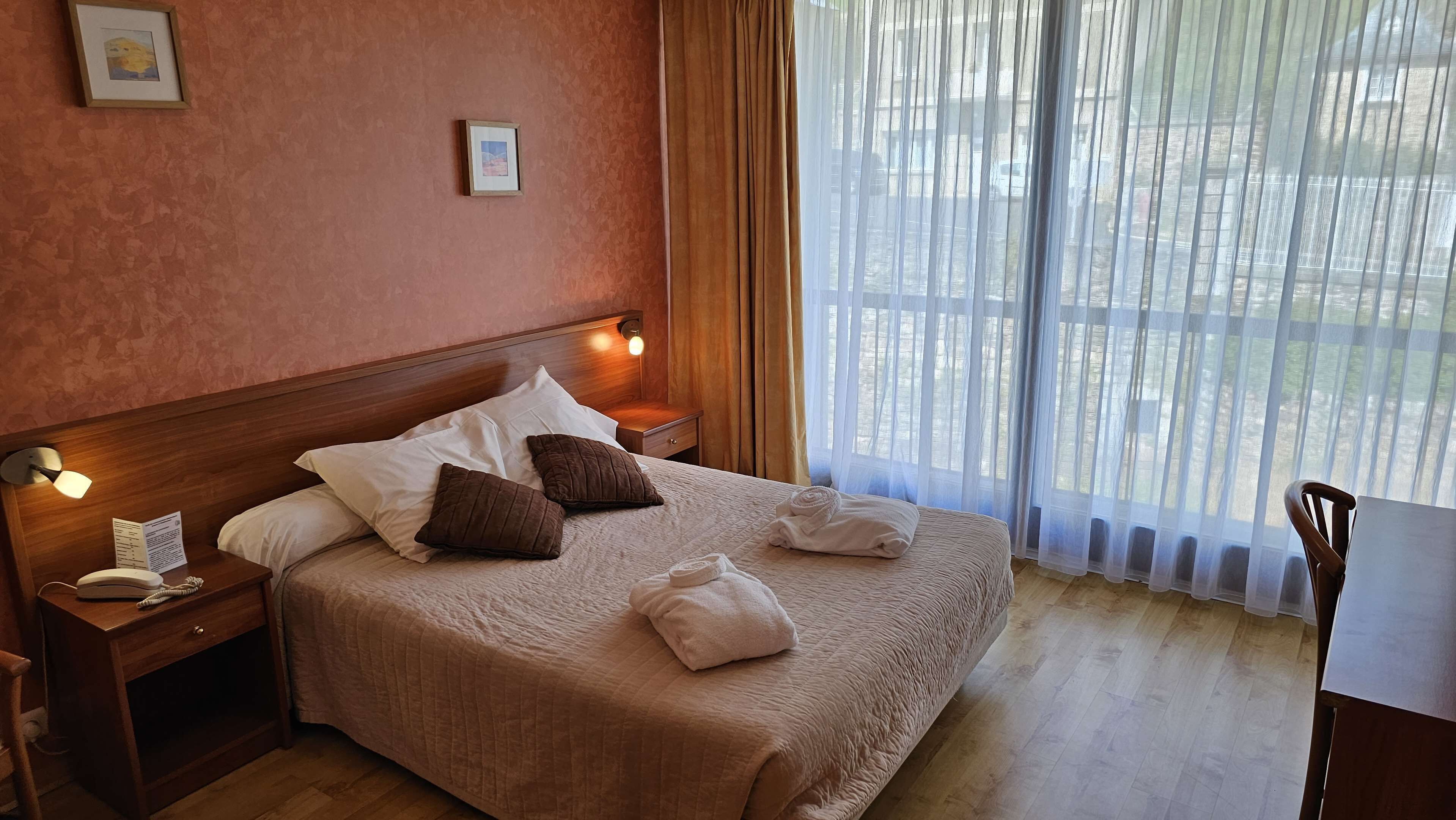 A neatly made bed with pillows, a bedside lamp, and a telephone on a wooden nightstand.