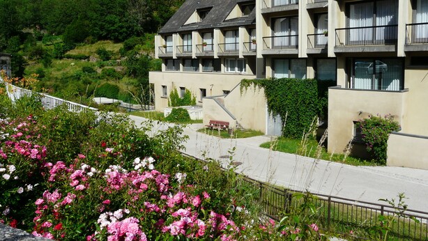 Un hôtel à plusieurs étages doté de balcons, situé sur une colline et surplombant un jardin parsemé de fleurs roses.