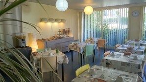 Un restaurant avec de nombreuses tables dressées pour le service, un espace buffet et de grandes fenêtres équipées de stores verticaux.