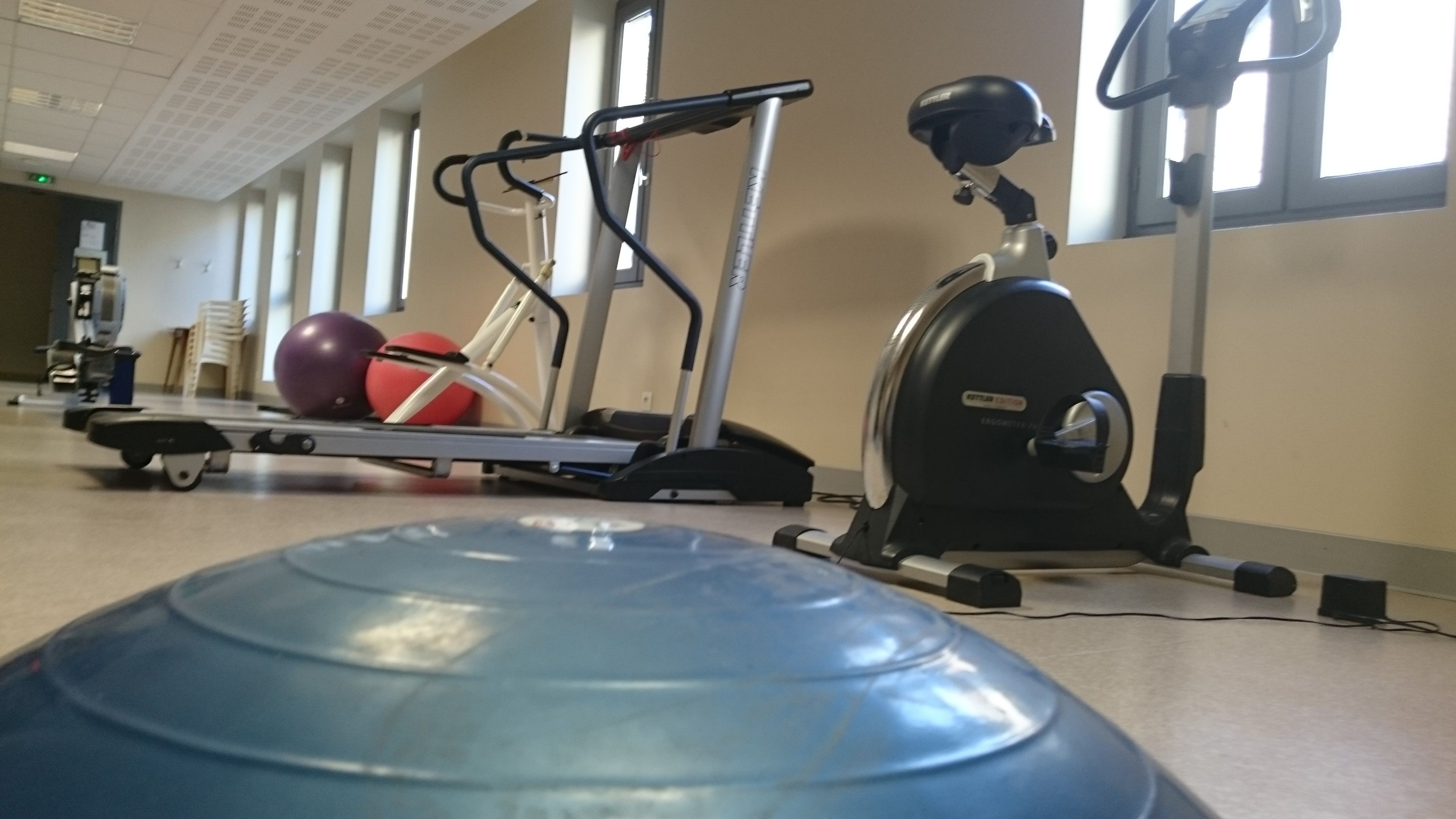 A gym with exercise equipment including a treadmill, elliptical, and a blue exercise ball.
