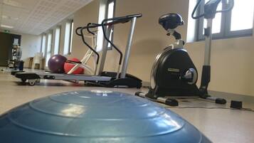 A gym with exercise equipment including a treadmill, elliptical, and a blue exercise ball.