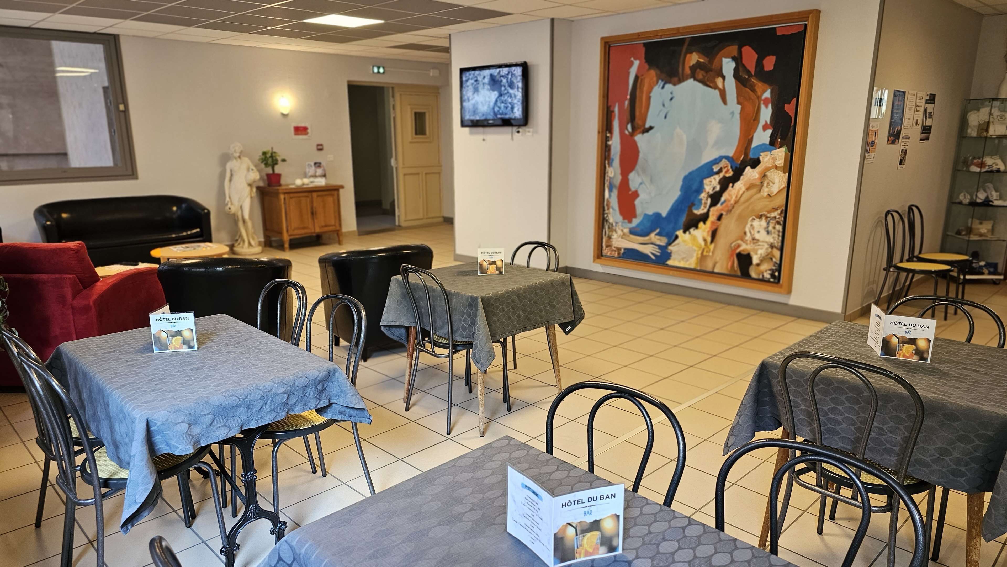Un bar de hotel con mesas y sillas, un televisor y un cuadro abstracto grande en la pared.