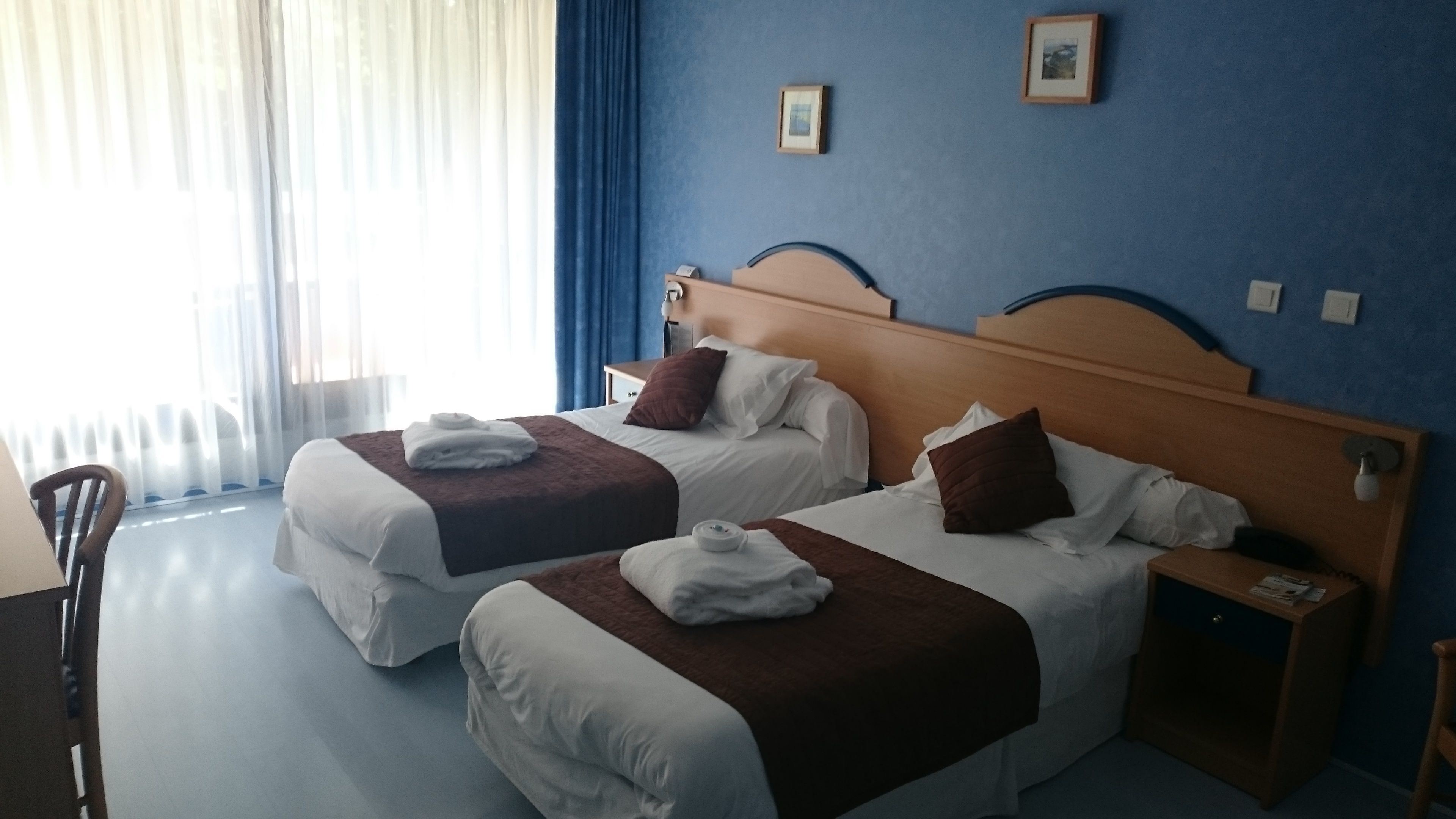 Une chambre d’hôtel avec deux lits, une tête de lit en bois, une table de chevet et une chaise.