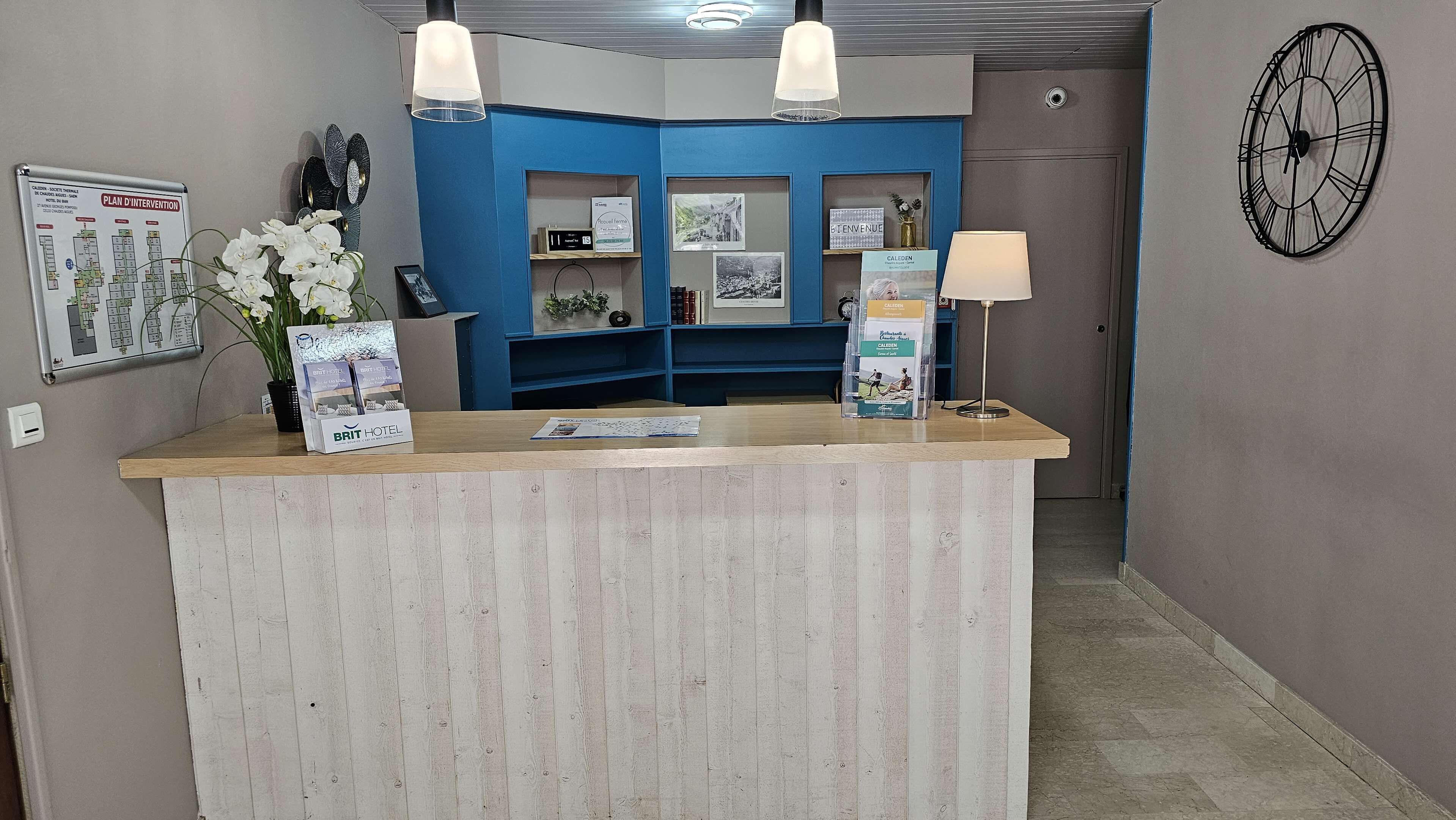 Un comptoir d’accueil avec un mur bleu, une horloge et un panneau d’accueil encadré.