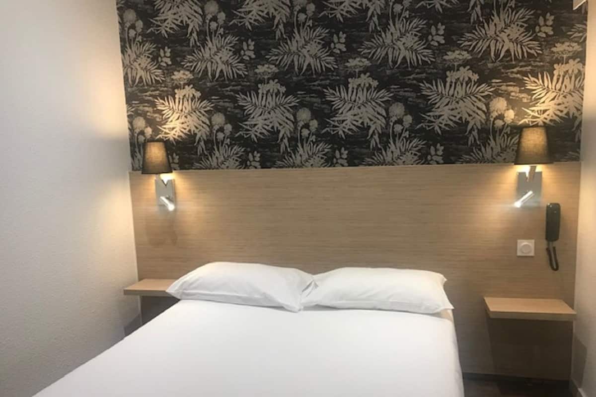 Une chambre d’hôtel comprenant un lit, deux tables de chevet, un téléphone fixé au mur et un éclairage décoratif mural.