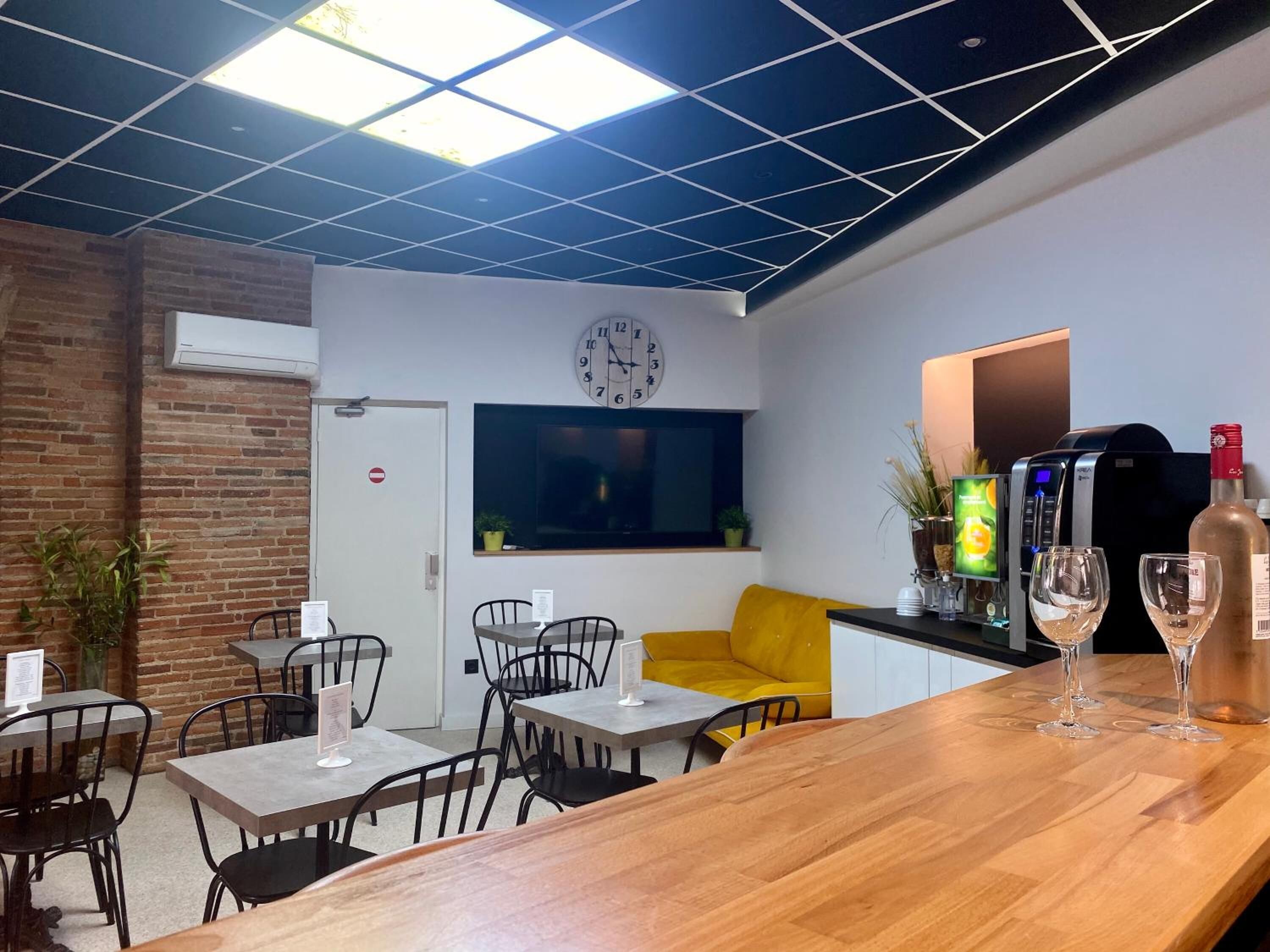 A modern cafe with a wooden bar, black chairs, a yellow sofa, and a clock on the wall.