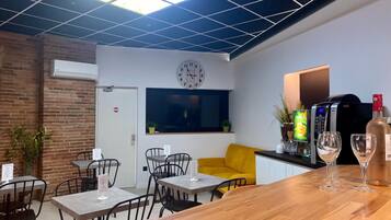 A modern cafe with a wooden bar, black chairs, a yellow sofa, and a clock on the wall.