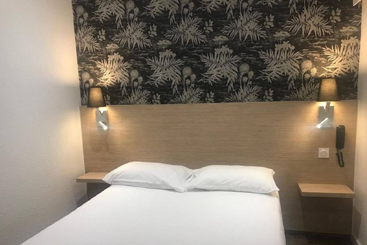 Ein Hotelzimmer mit einem Bett, zwei Nachttischen, einem an der Wand befestigten Telefon und zwei Wandleuchten.