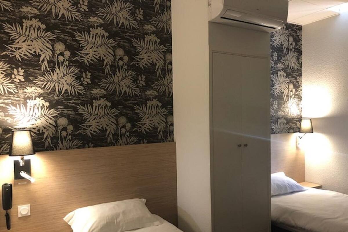 Ein Hotelzimmer mit zwei Betten, einem gemusterten Wandteppich und Nachttischlampen.