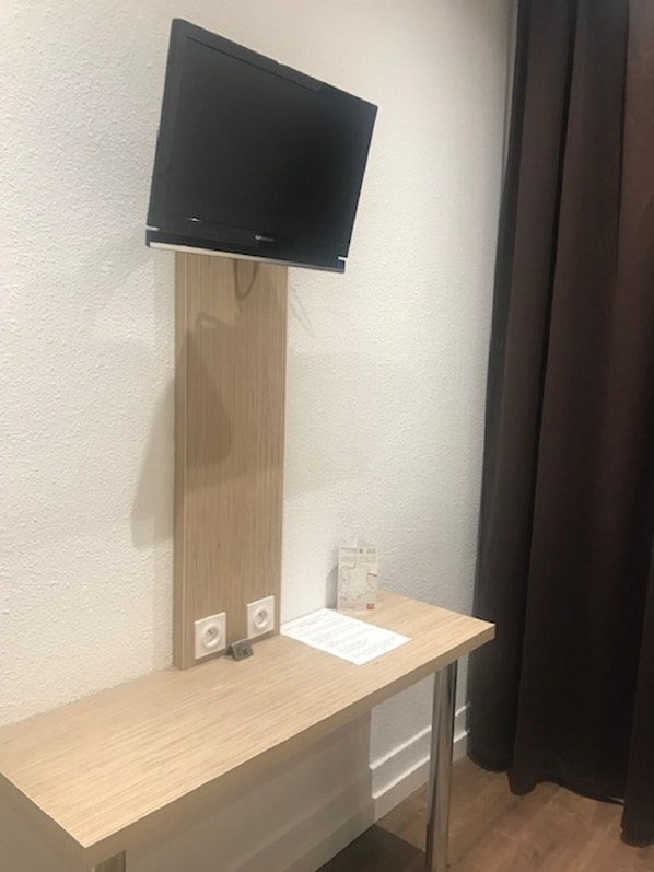 A room with a wooden desk, a mounted flat-screen TV, and a small whiteboard.