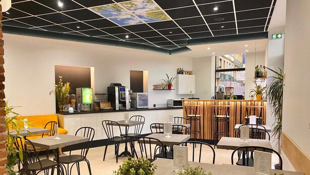 Een modern café met een bar, zitplaatsen en een plafond met een geometrisch patroon.