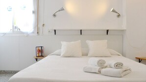 Un letto rifatto con lenzuola e cuscini bianchi, un comodino con una cornice e due lampade a parete.
