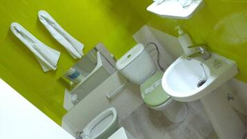 A bathroom with a green wall, a toilet, a bidet, a sink, and two towels.