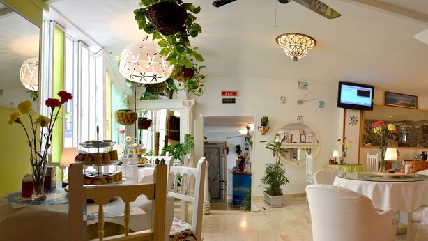 Un'ampia sala da pranzo con sedie e tavoli bianchi, un lampadario e piante sospese.