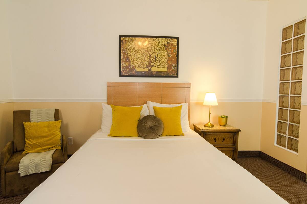 Une chambre d’hôtel avec un grand lit, une chaise, une table de chevet avec une lampe et une œuvre d’art encadrée au mur.
