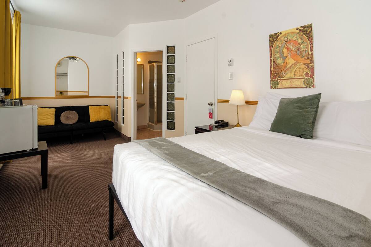 Une chambre d ’hôtel avec un lit, un bureau, une chaise, un miroir, une porte et un mur orné d’un tableau.