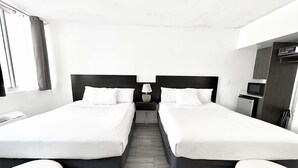 A hotel room with two single beds, a small desk with a lamp, a TV, and a minibar.