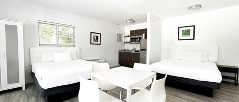 A modern hotel room with two beds, a small kitchenette, a dining area, and a bathroom.