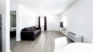 A modern, minimalist living room with a sofa, a TV, and a dining area.