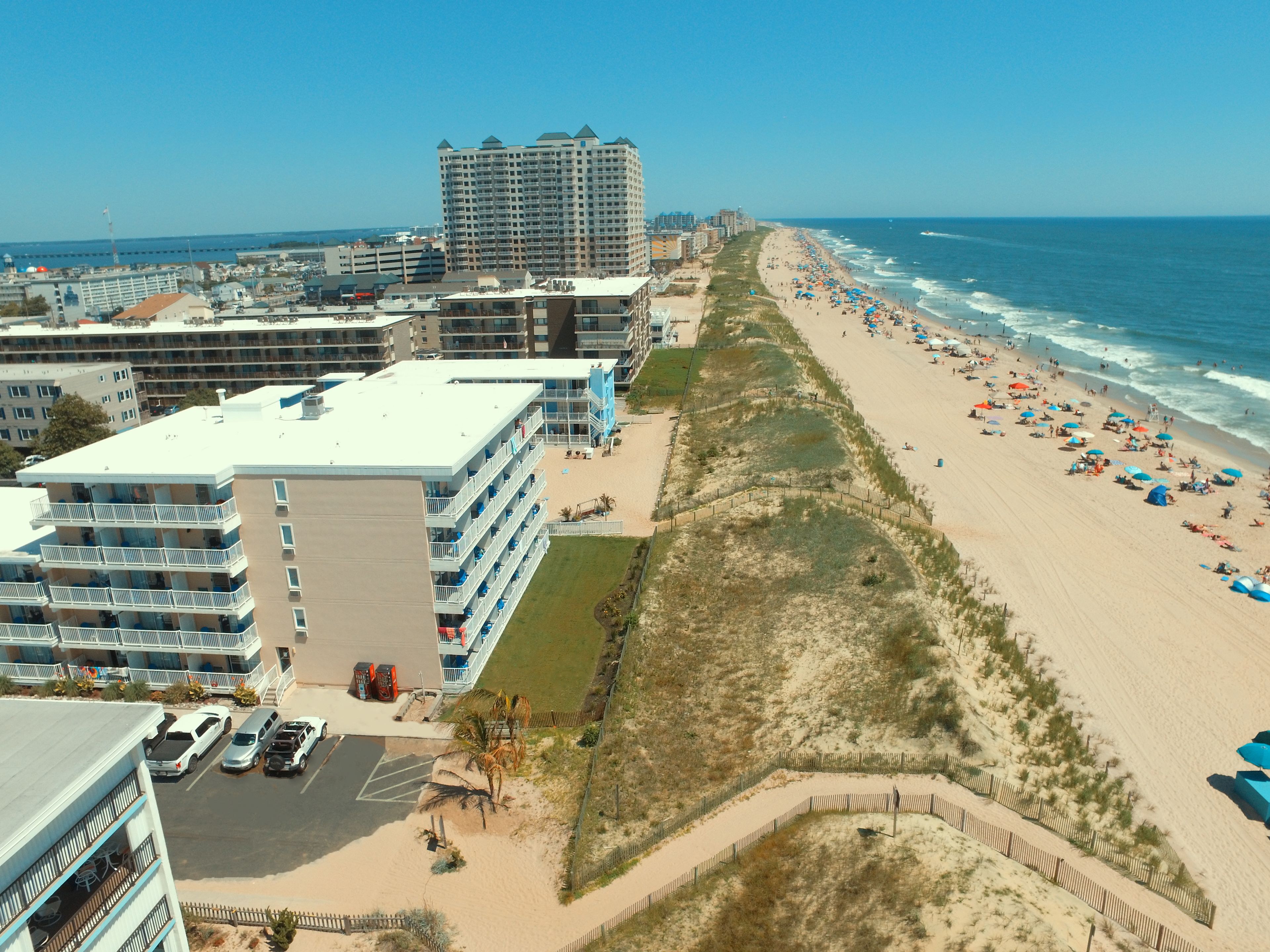 Un hôtel situé en bord de mer, avec plusieurs étages, un parking et une plage de sable équipée de parasols.