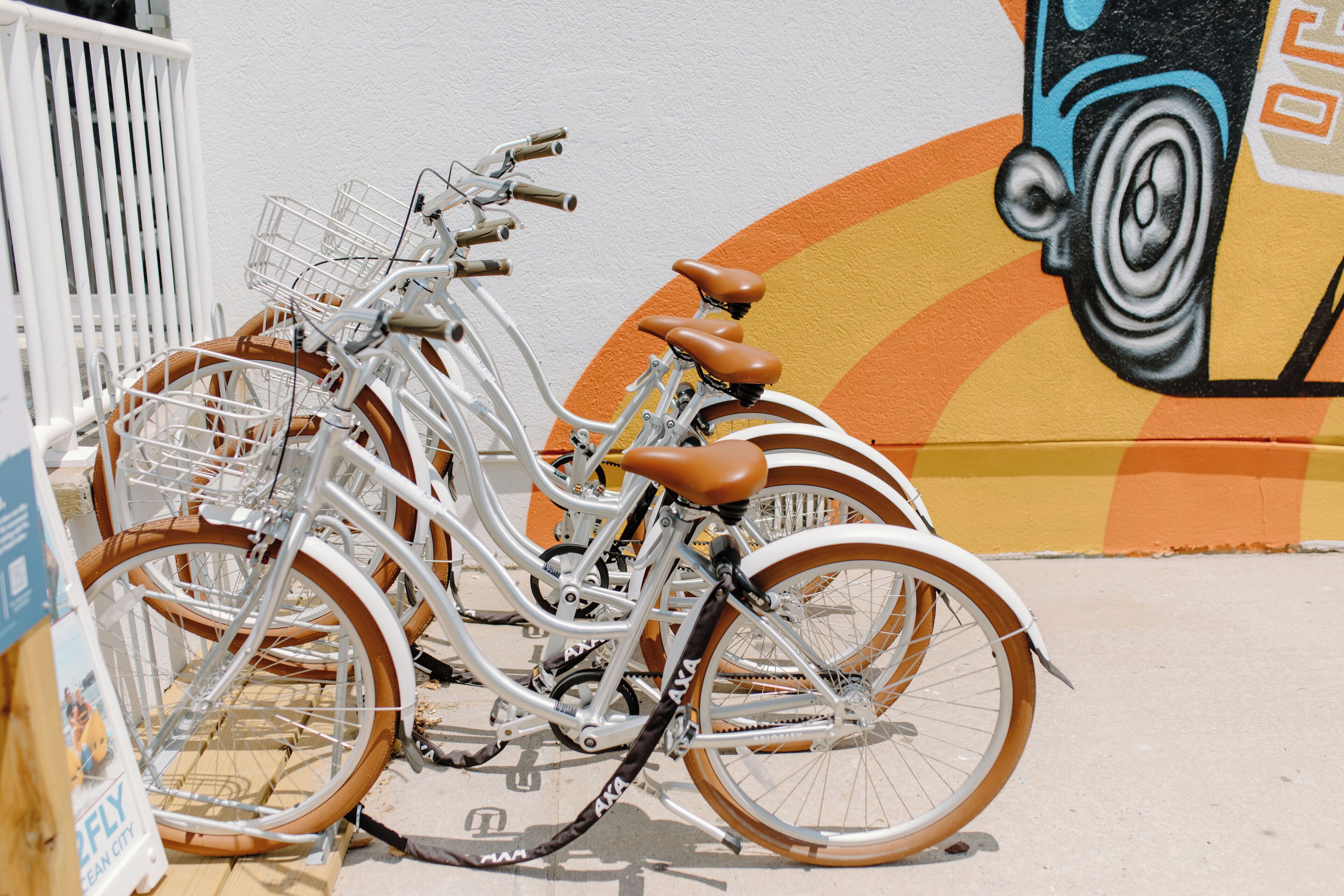 A bicycle with a basket and brown seats parked against a wall with a mural.