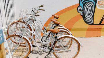 Una bicicleta con cesta y asientos marrones estacionada frente a un muro con un mural.