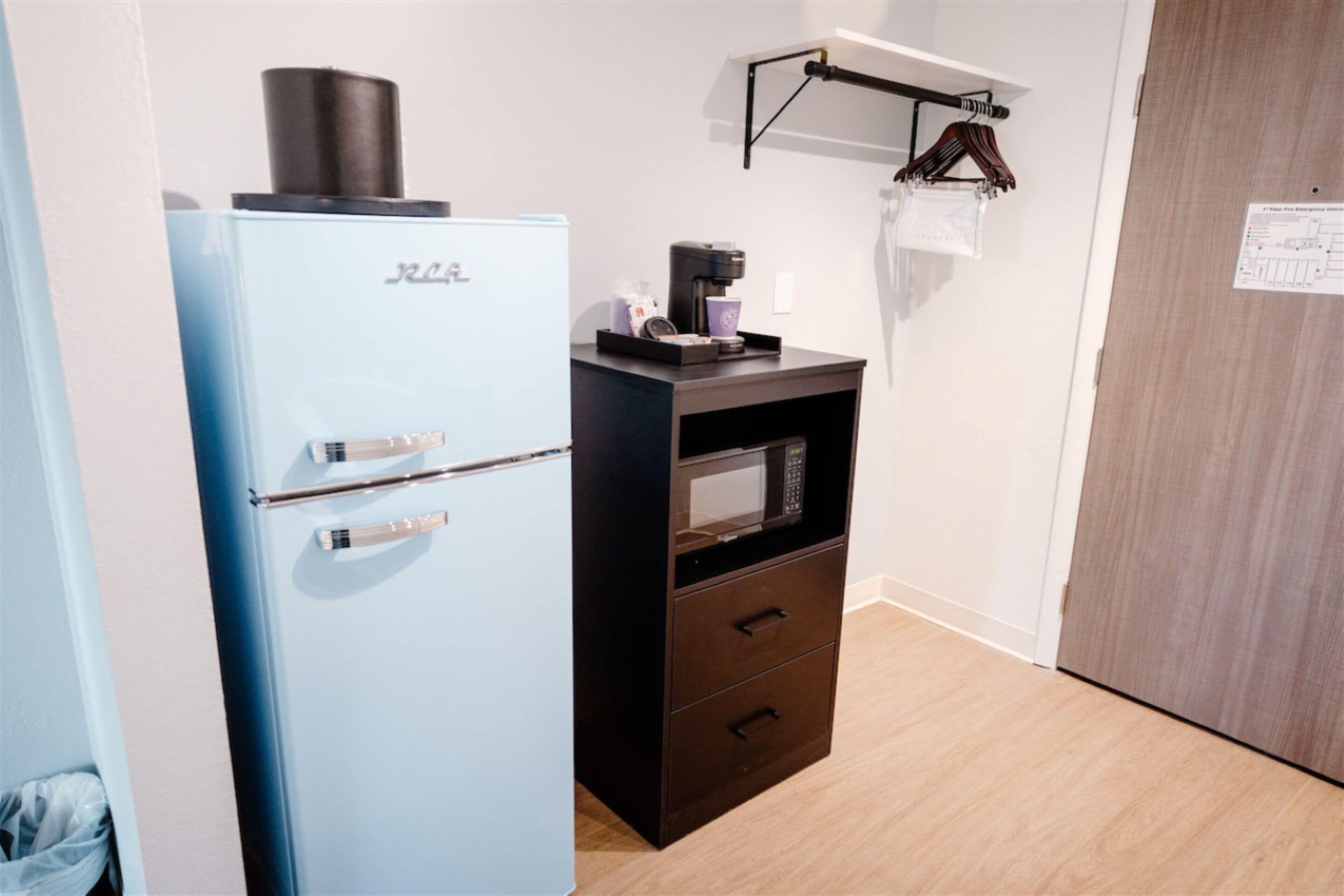 Una kitchenette compacta con un refrigerador azul, un microondas y una cafetera sobre una pequeña encimera.