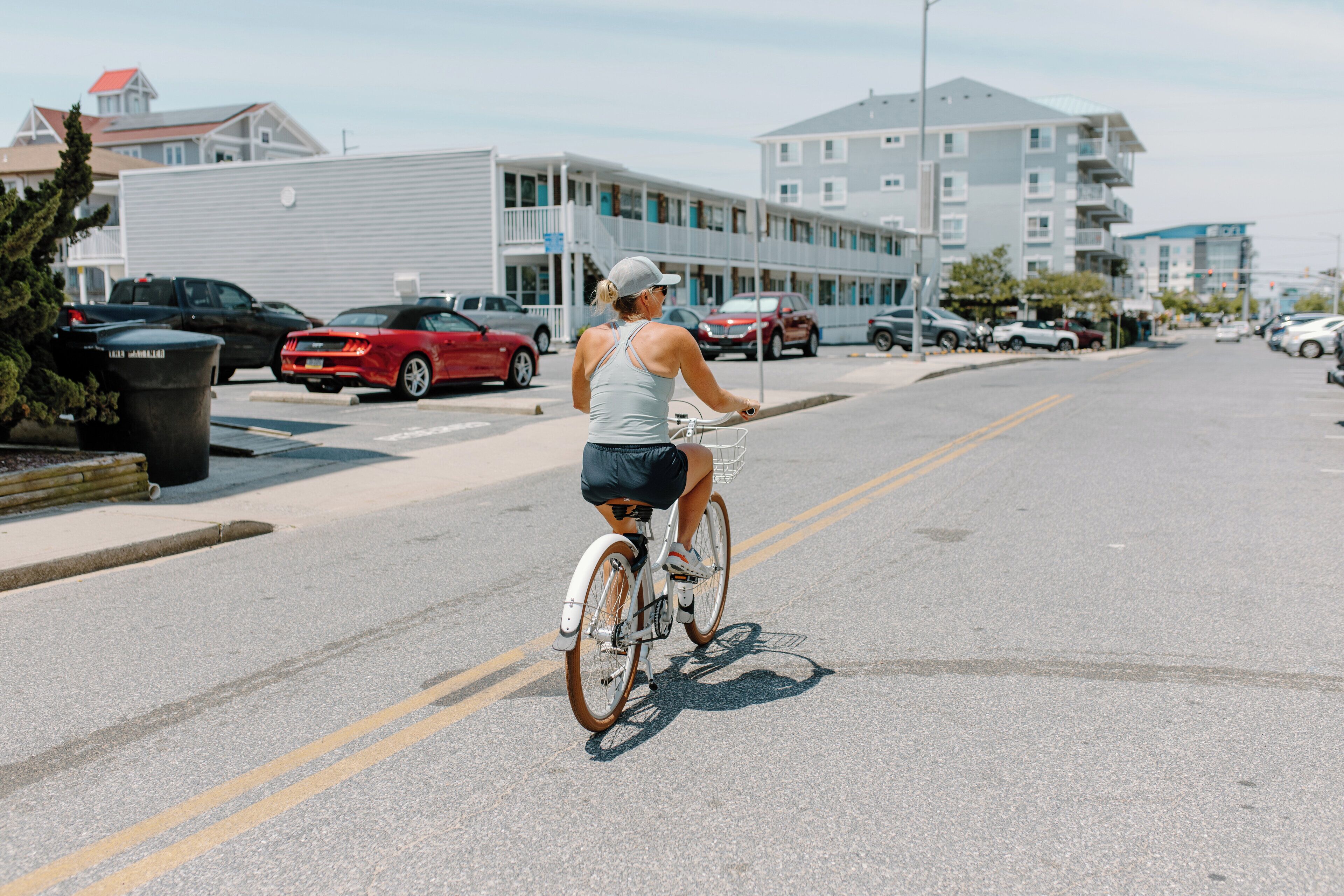 A woman riding a bicycle on a street with parked cars and buildings in the background.