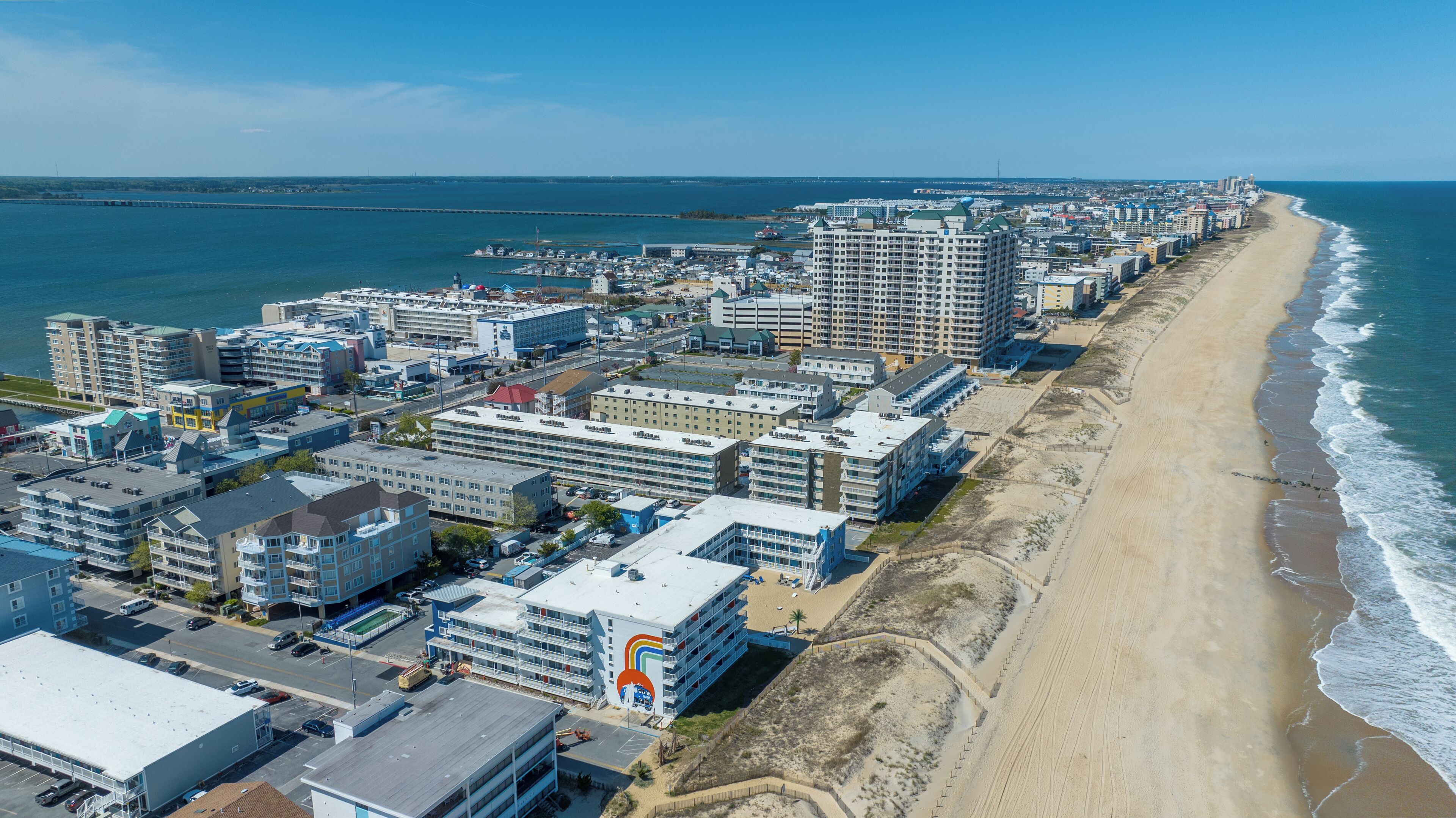 Un paysage urbain côtier avec un hôtel situé en bord de mer, comprenant plusieurs étages, un parking et une vue sur l’océan.