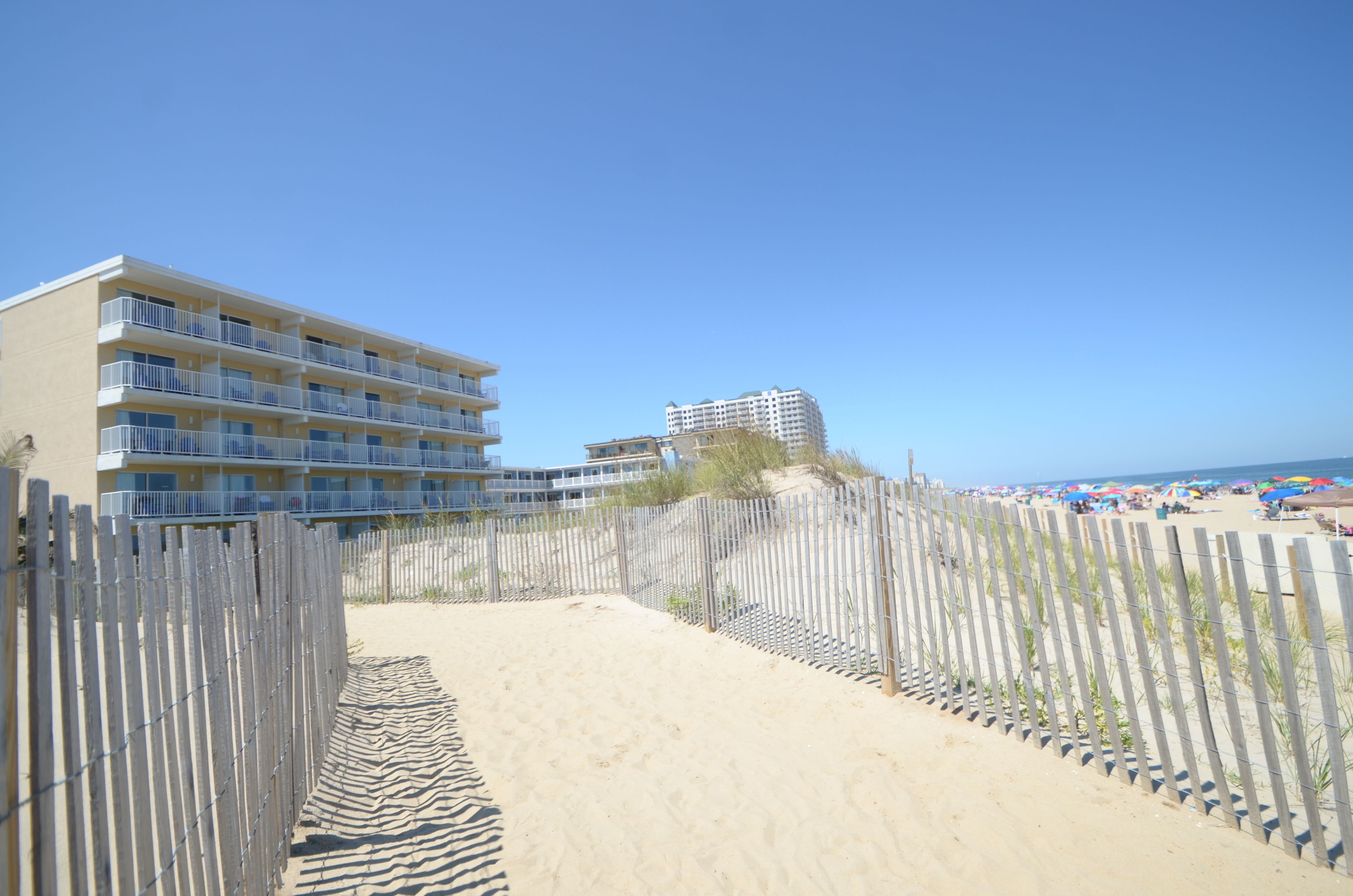 A beachfront hotel with multiple balconies and a sandy path leading to the beach.