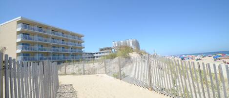 A beachfront hotel with multiple balconies and a sandy path leading to the beach.