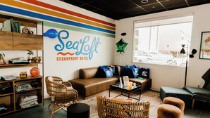 Un vestíbulo moderno de hotel con un gran letrero en la pared que dice "SeaLoft Oceanfront Hotel", muebles de mimbre, un sofá de cuero y vistas de la calle a través de un ventanal.