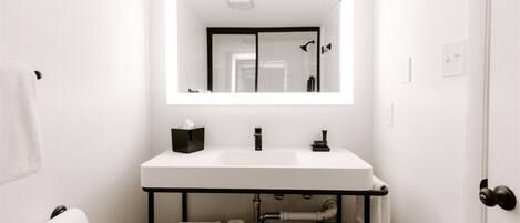 Un bagno moderno con lavandino bianco, uno specchio e un porta asciugamani.
