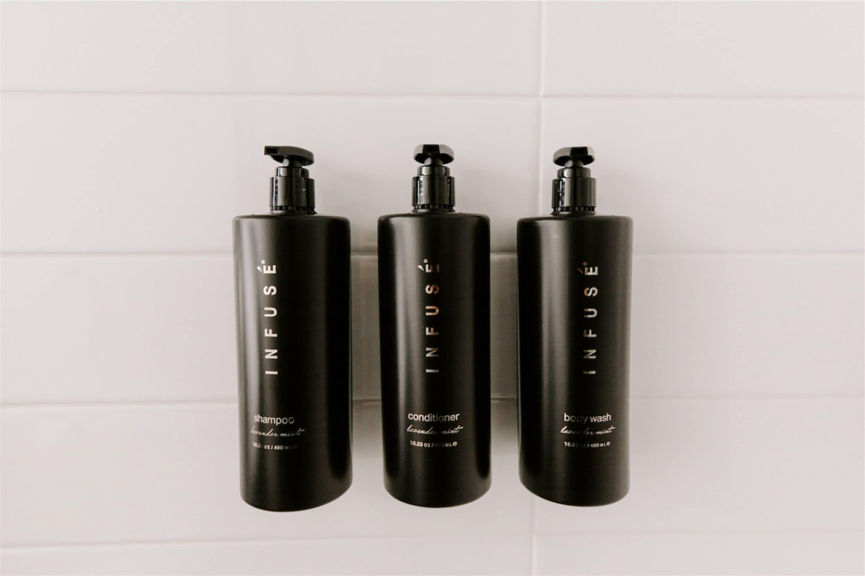 Trois bouteilles noires de la marque INFUSE, contenant respectivement du shampooing, de l’après-shampooing et du gel douche.