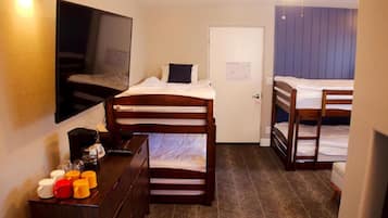 A compact hotel room with a single bed, a dresser with mugs, a ceiling fan, and a door with a notice.
