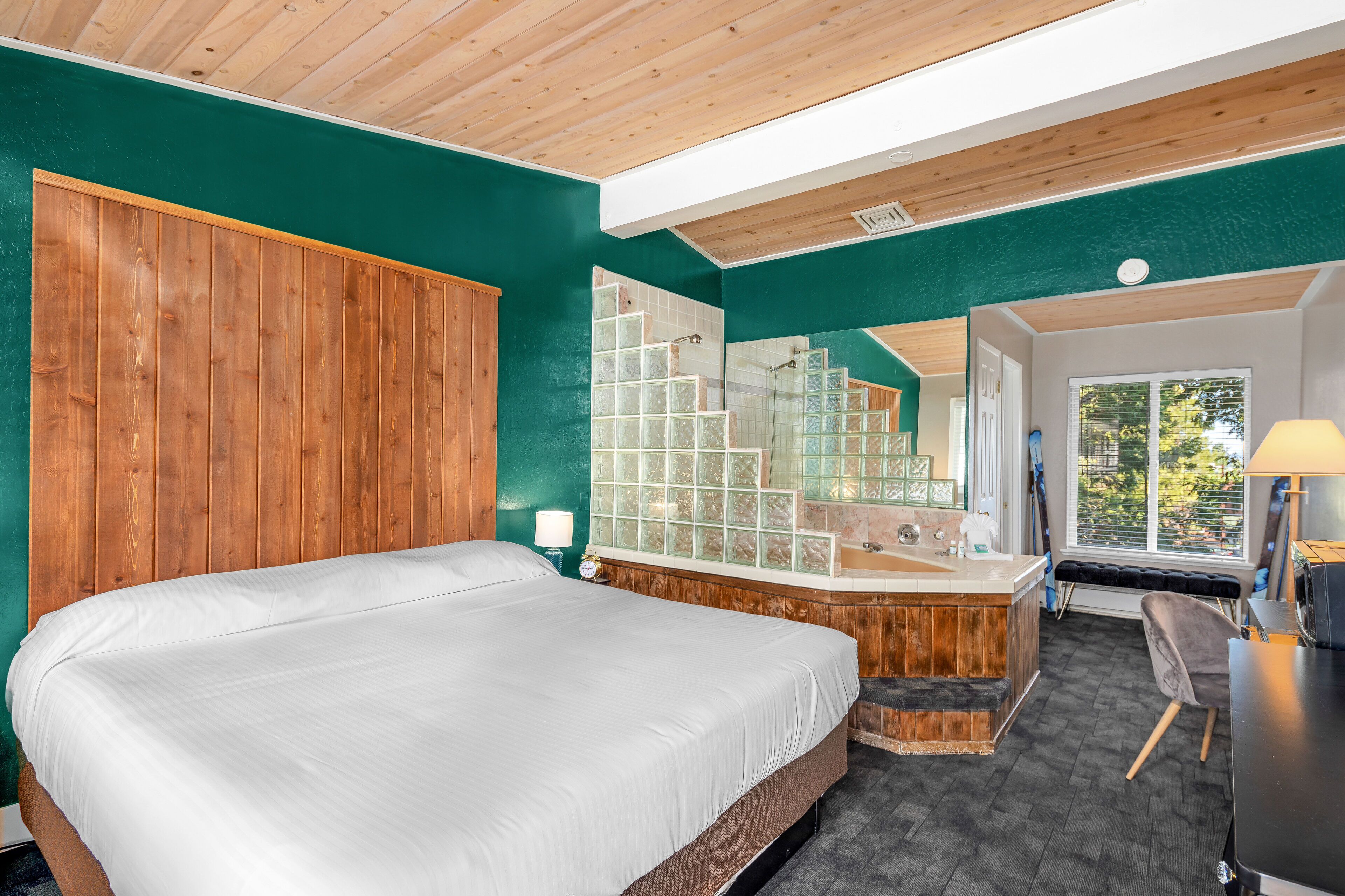 A bedroom with a large bed, a wooden headboard, a bathroom with a glass shower, and a view of the outdoors.