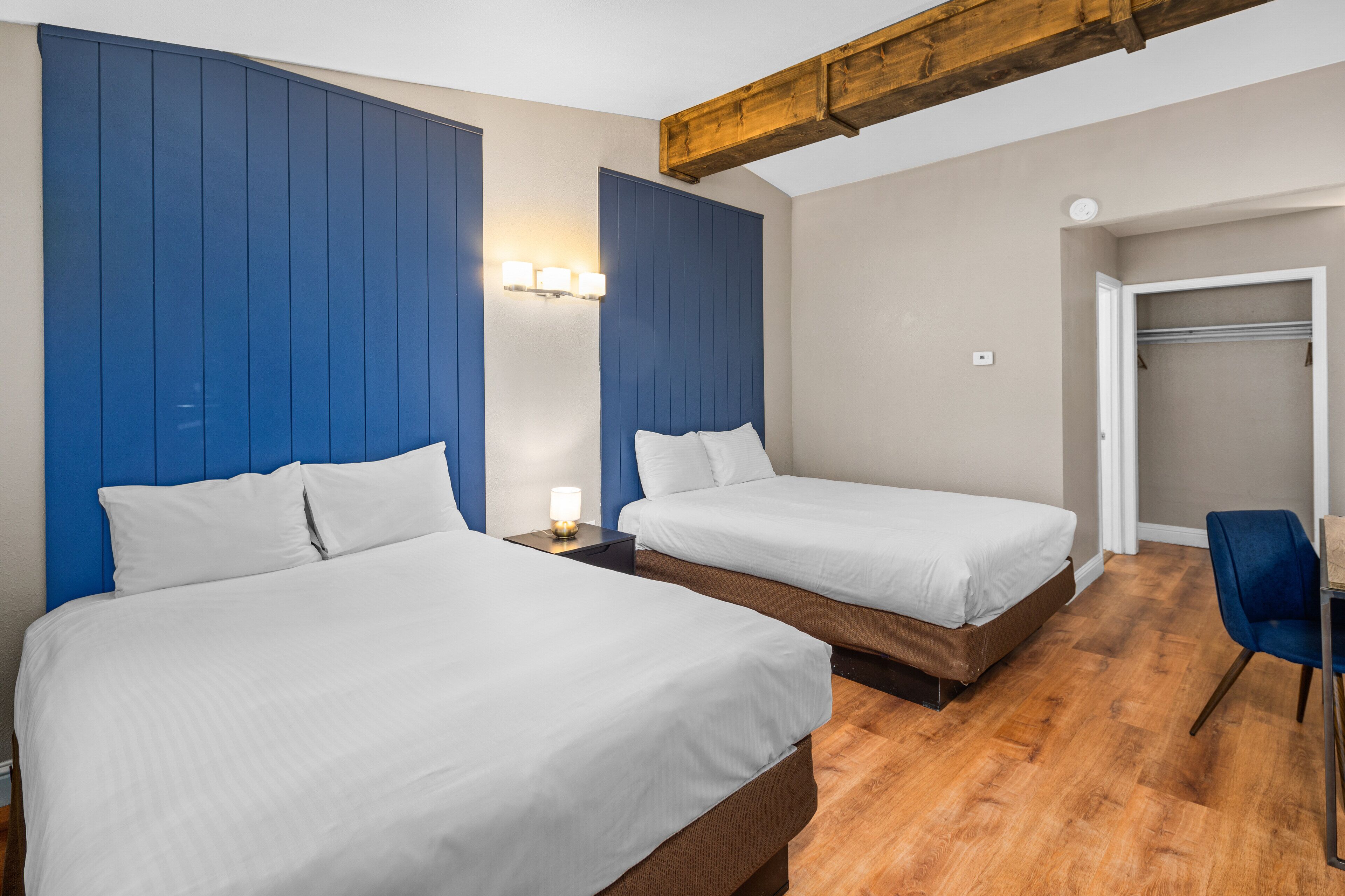 Habitación de hotel con dos camas, suelo de madera y una pared azul de detalles.