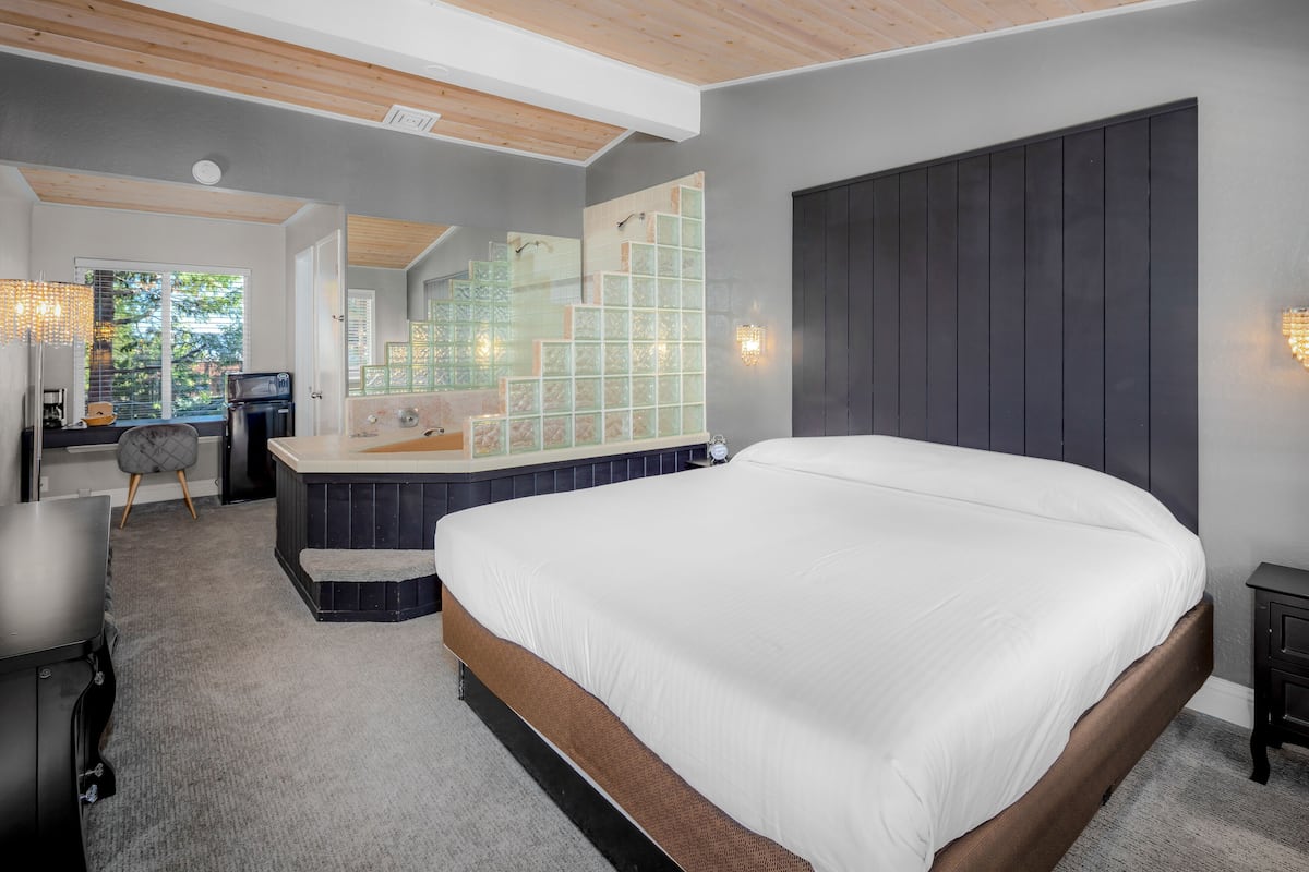Une chambre moderne dotée d’un grand lit, d’une baignoire intégrée et d’un coin salon offrant une vue sur l’extérieur.