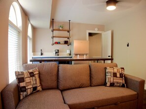 A cozy living area with a brown sectional sofa, a coffee machine, a lamp, and a small shelf with decorative items. - The Inn at Boatworks (Tahoe City)