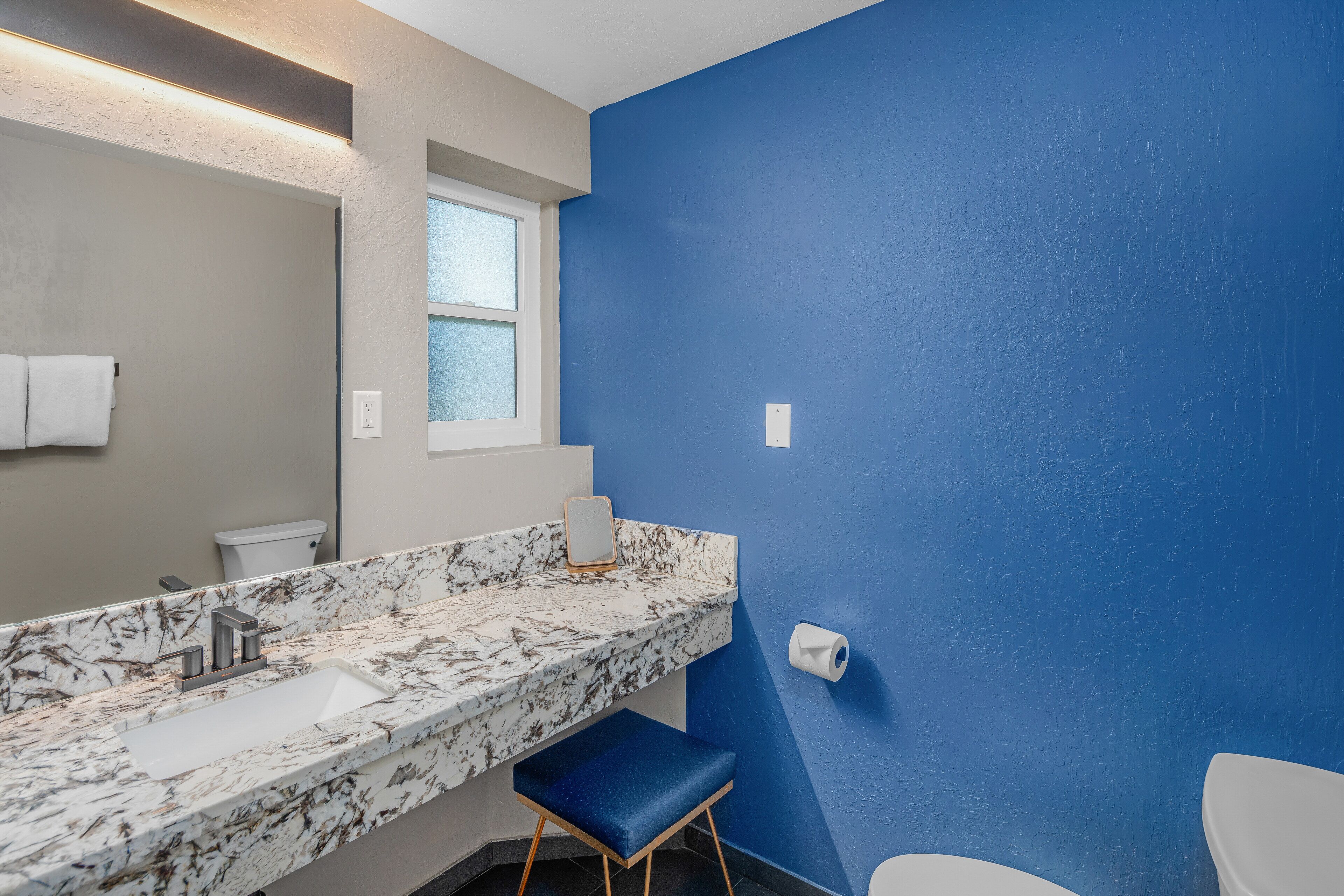 Ein Badezimmer mit Marmorwaschbecken, blauer Wand, Toilette und Fenster.
